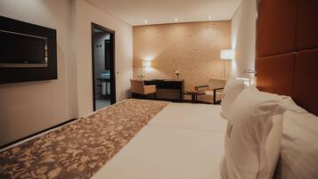 Habitación de hotel con cama, escritorio, dos sillas, televisor y lámpara.