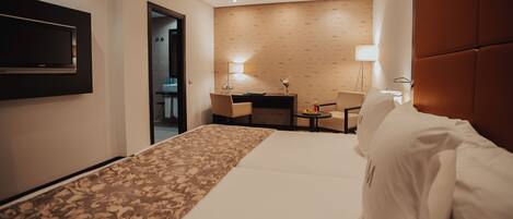 Habitación de hotel con cama, escritorio, dos sillas, televisor y lámpara.
