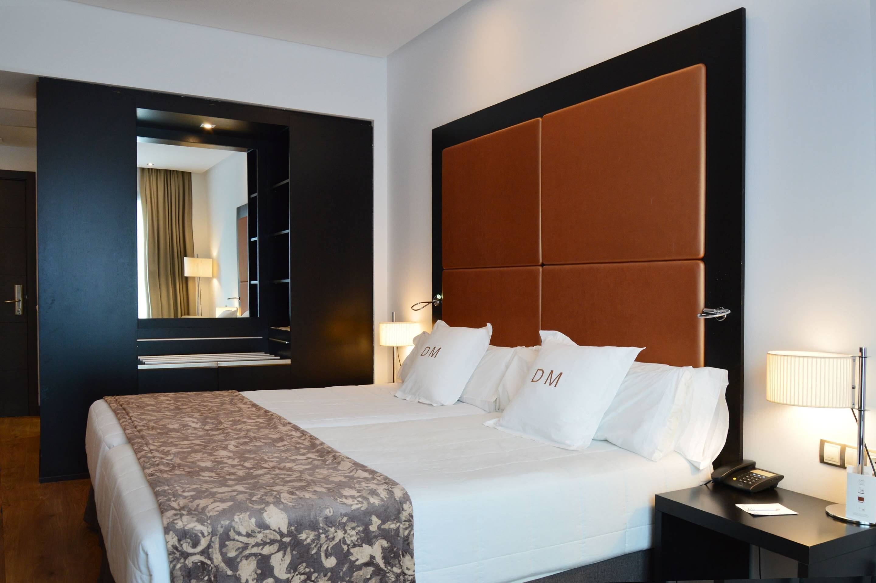 A hotel room with a large bed, a headboard, two bedside lamps, a bedside phone, and a nightstand.