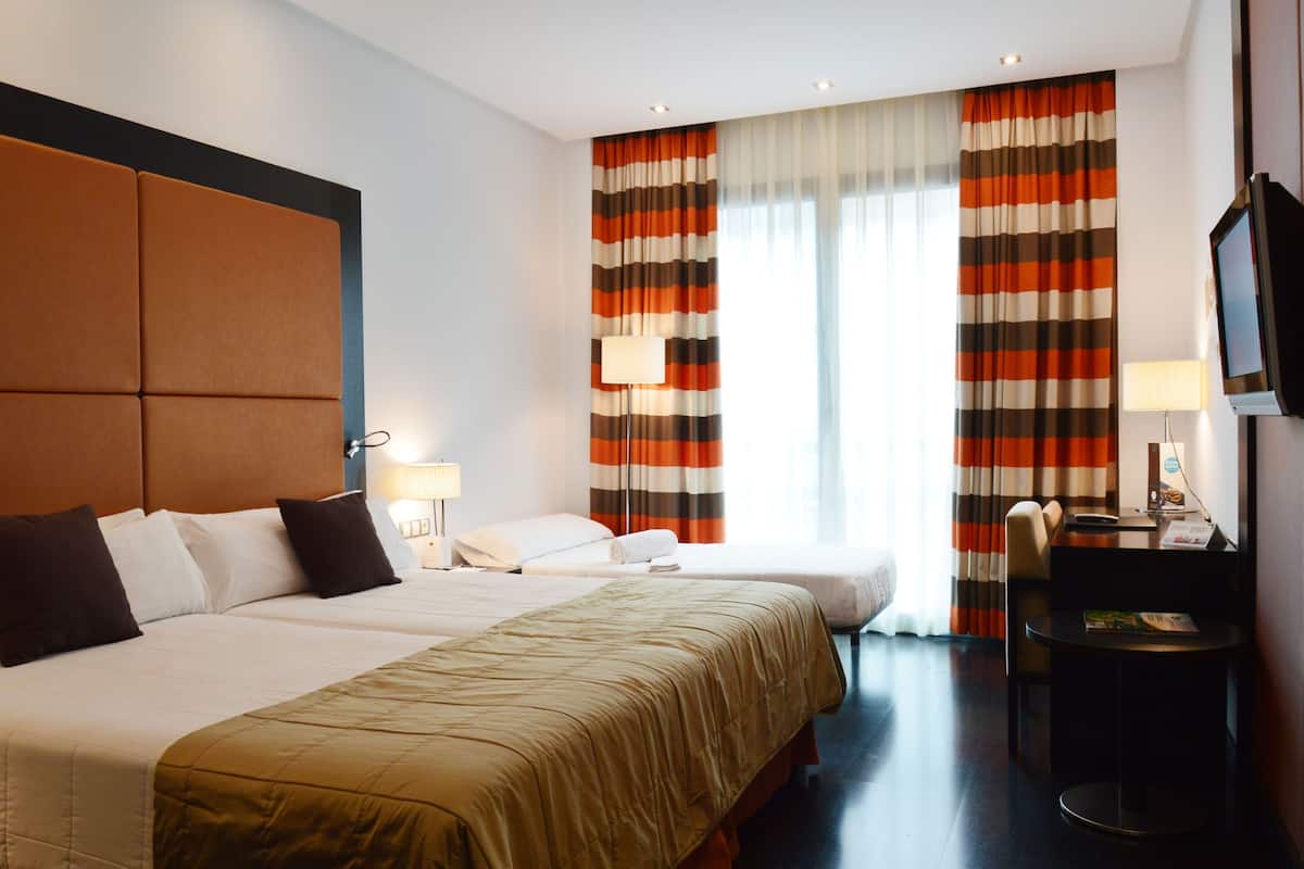 A hotel room with two beds, a desk with a chair, a television, and striped curtains.