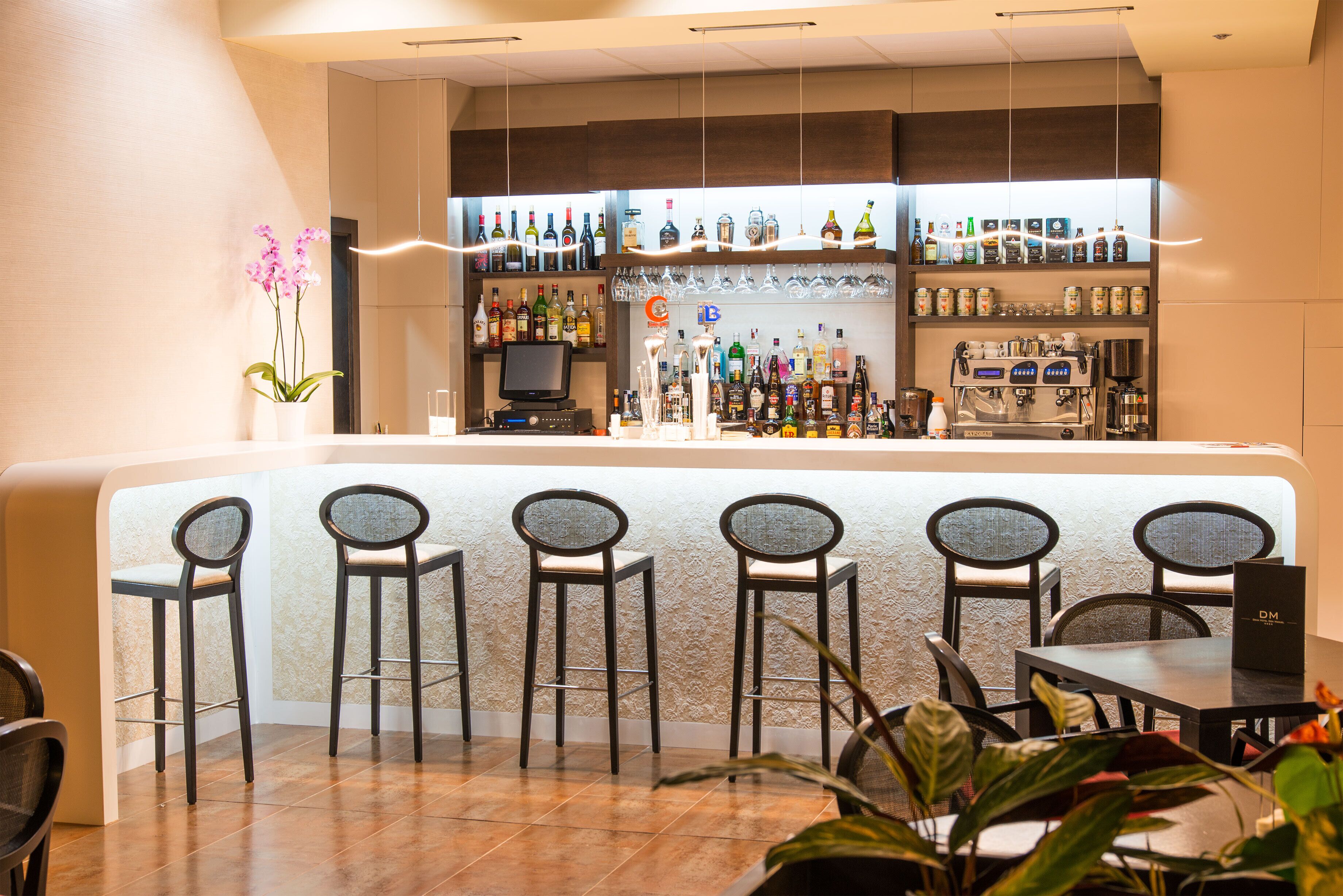 A bar area with a counter, bar stools, a coffee machine, and shelves with bottles and glasses.