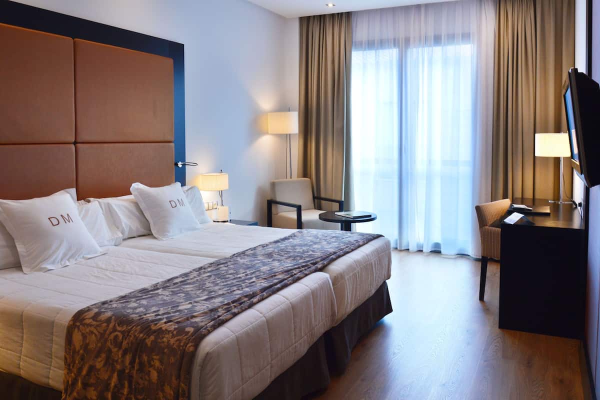 A hotel room with a large bed, a desk, a chair, a TV, and a window with curtains.