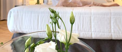 A hotel room with a bed, a bedside table, and a clear glass vase with white flowers.