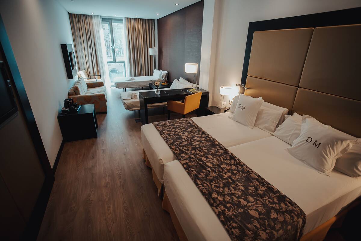 A hotel room with a large bed, a desk, a sofa, and a view of the city.