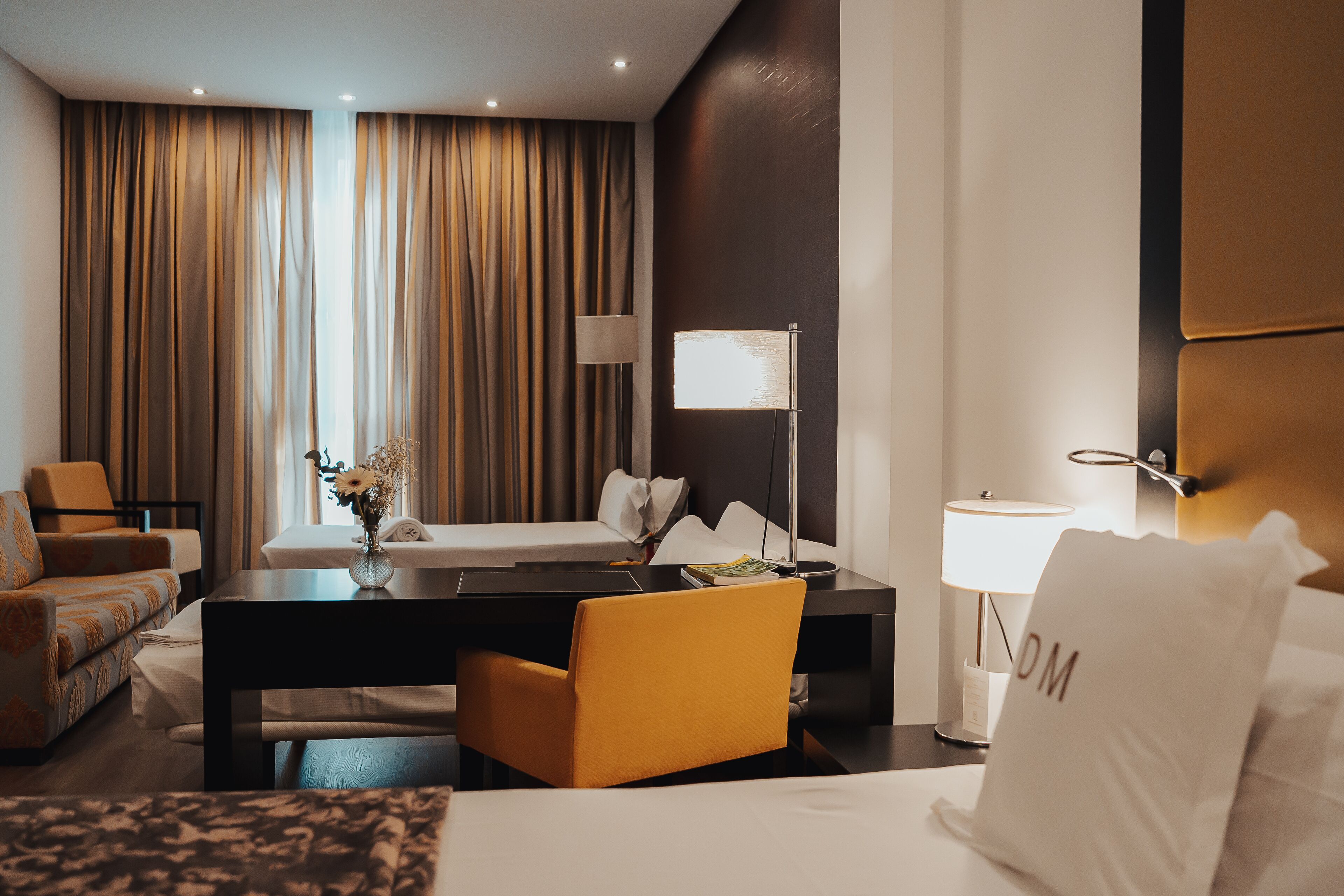 Una habitación de hotel con cama, escritorio, silla, lámpara y cortinas.