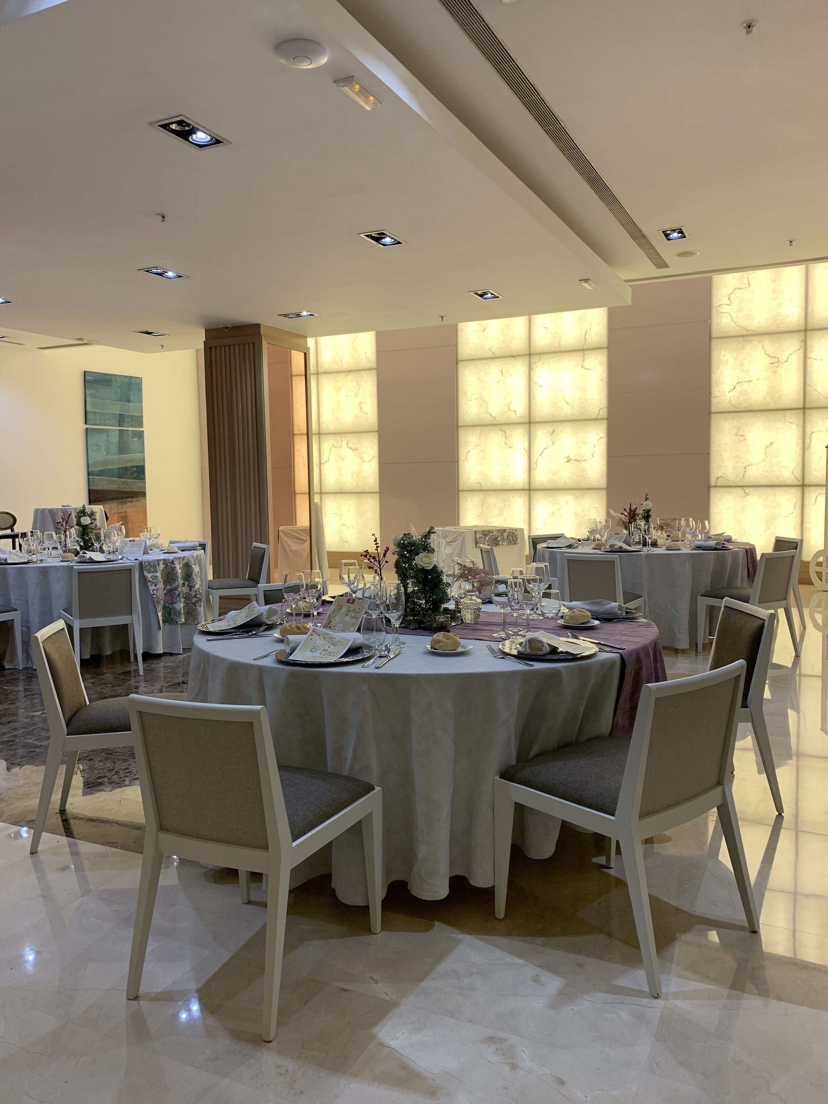 Un comedor bien iluminado con mesas redondas dispuestas para una comida, con manteles blancos y sillas.