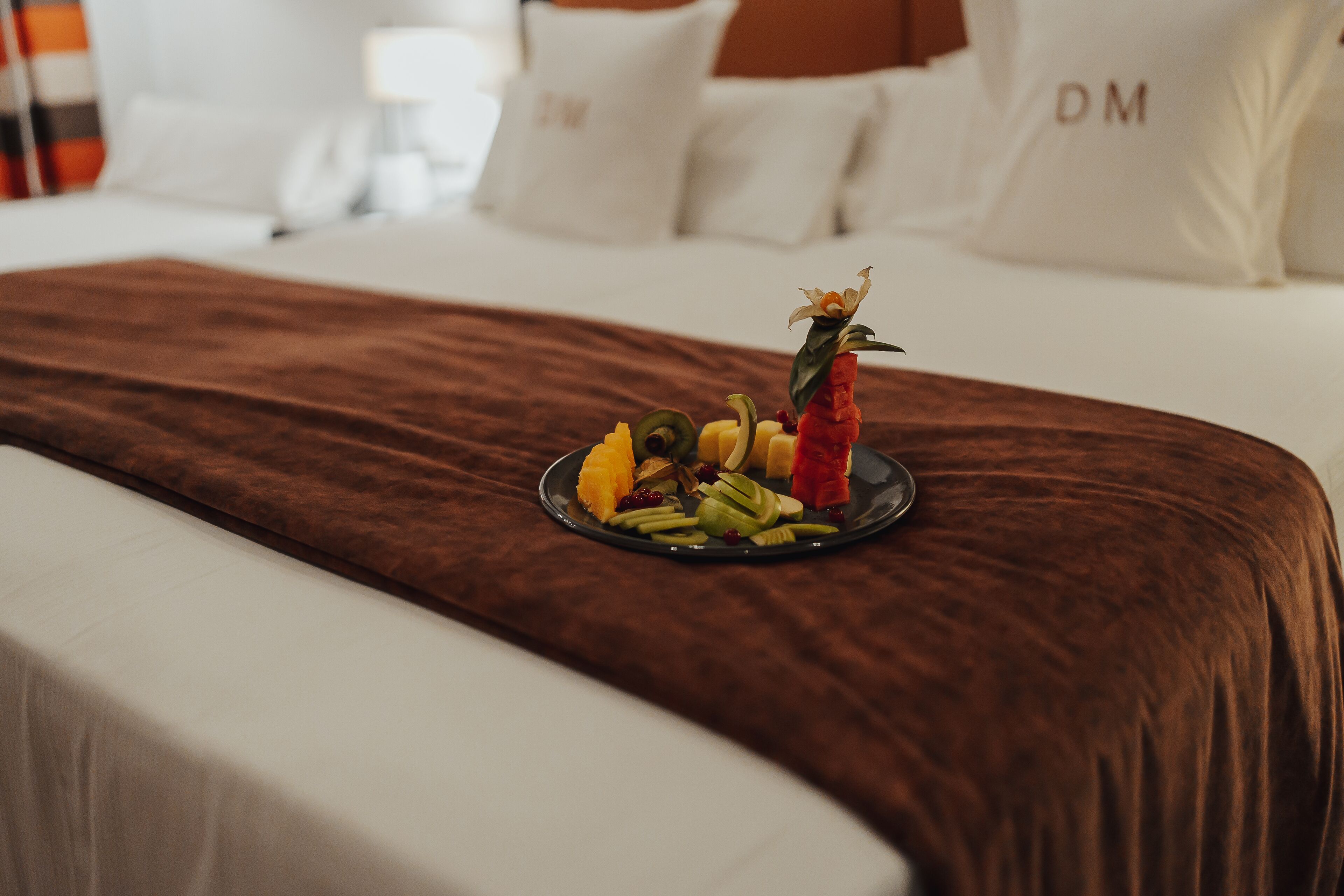 Una cama bien hecha con una colcha marrón y un plato de fruta al lado.