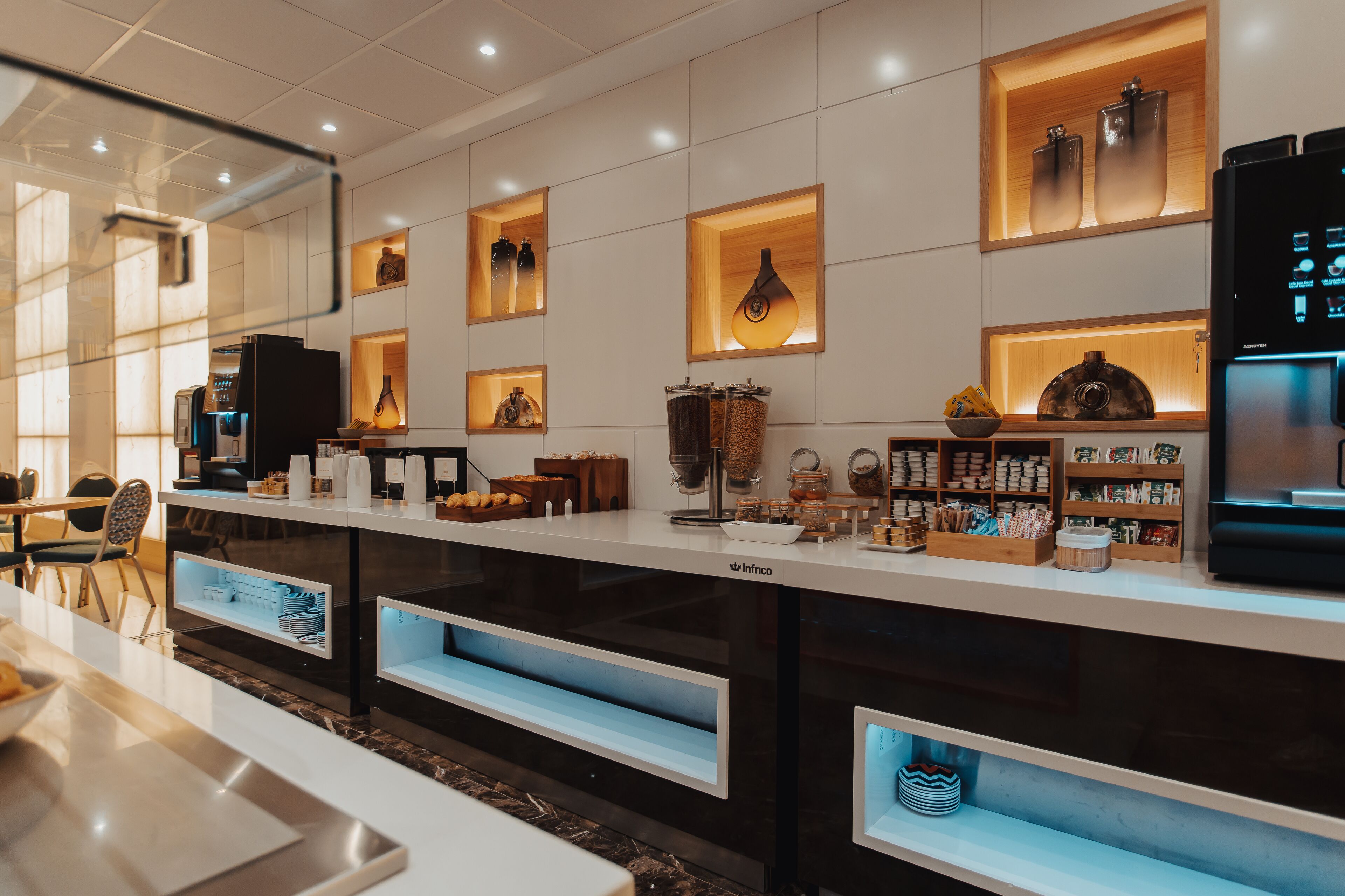 A modern hotel lobby with a long reception counter, shelves with various items, and a coffee machine.
