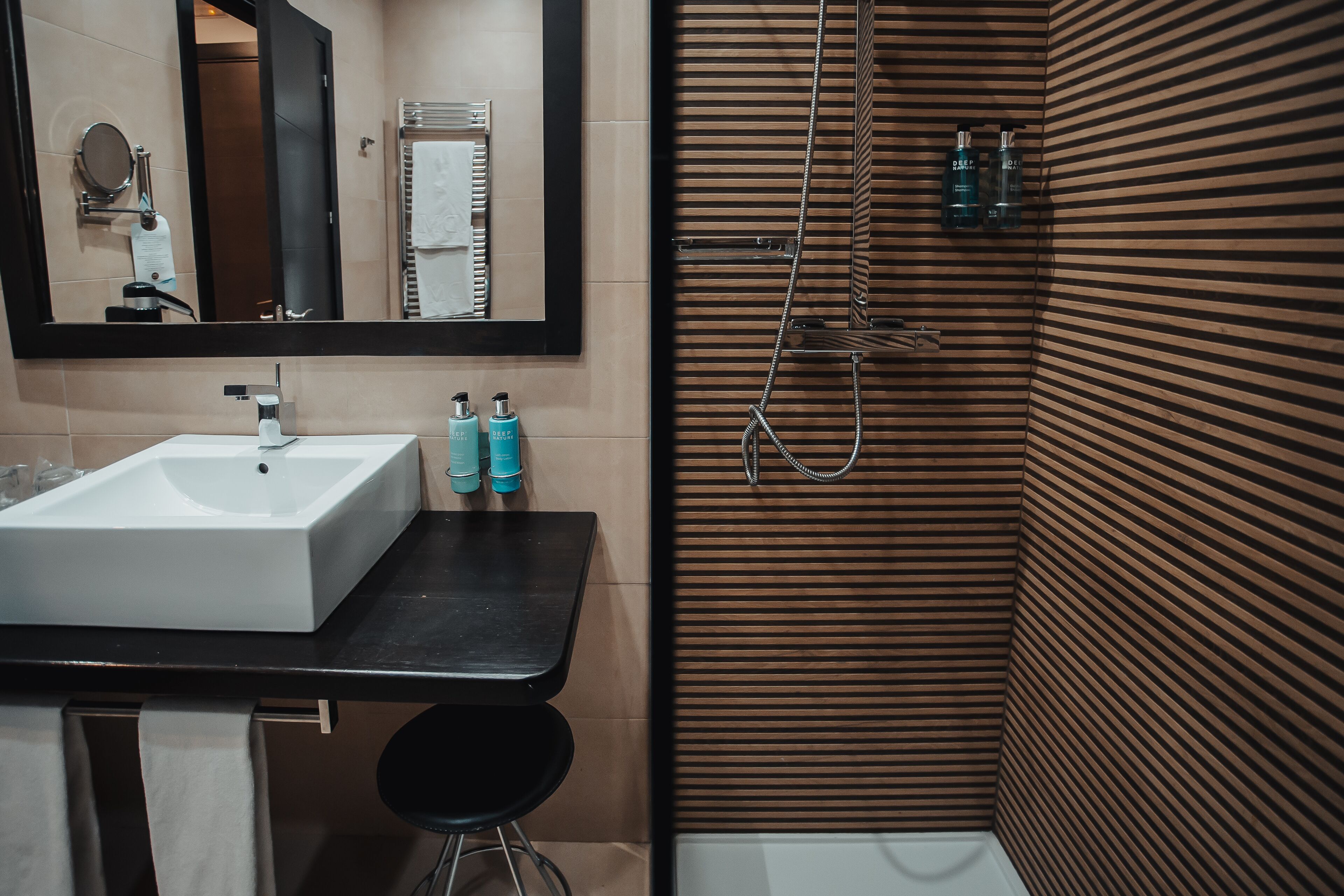 A bathroom with a white sink, mirror, and towel rack. There are two bottles on the counter.