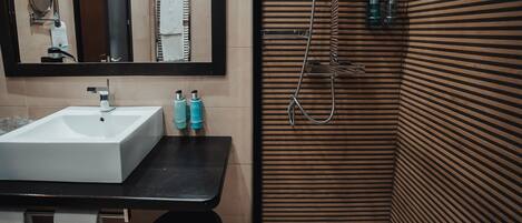 Un baño con lavamanos blanco, espejo y barra para toallas. Hay dos botellas sobre la encimera.