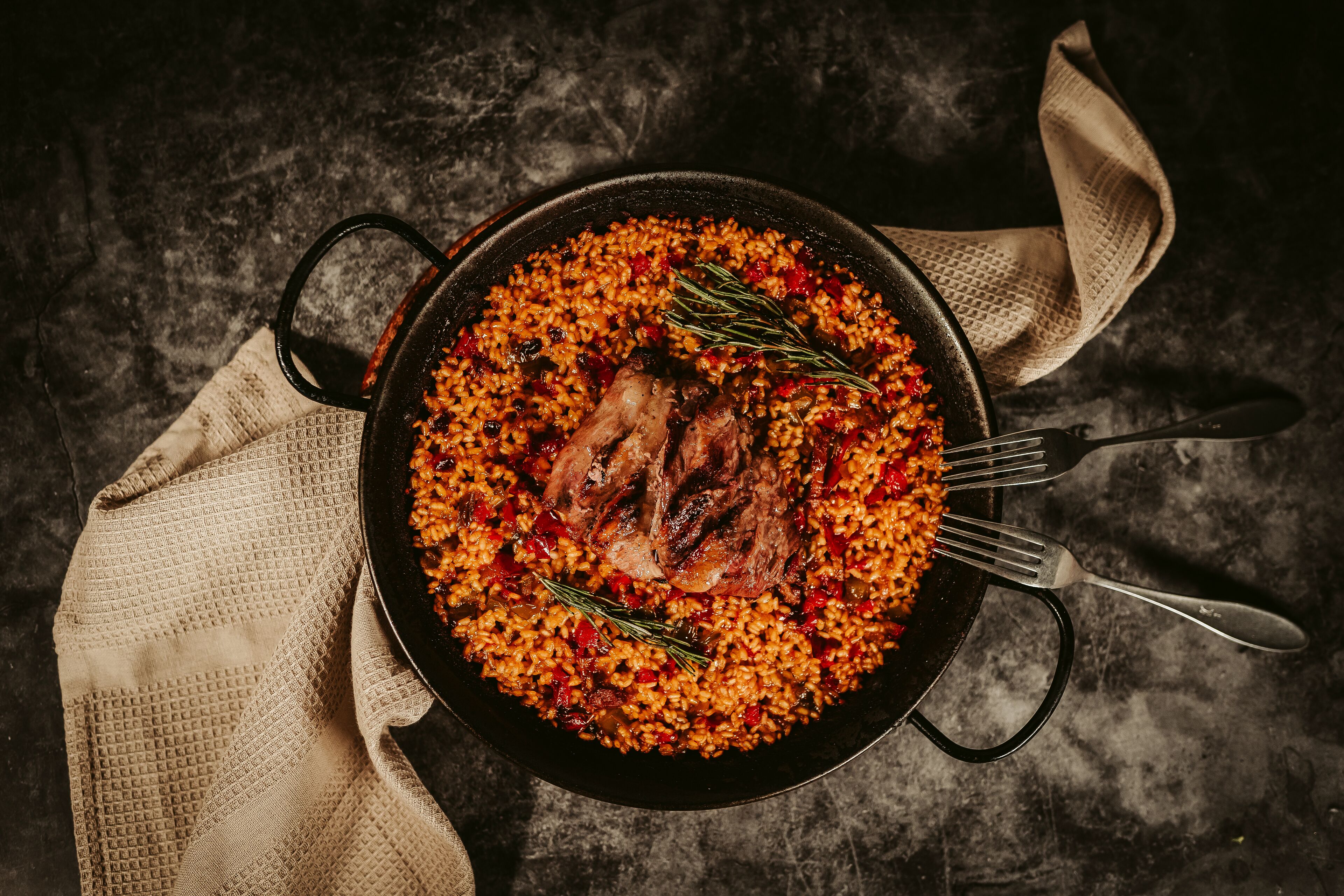 Un plat de riz agrémenté de viande et de légumes, une fourchette et une serviette en tissu, le tout posé sur une surface sombre.