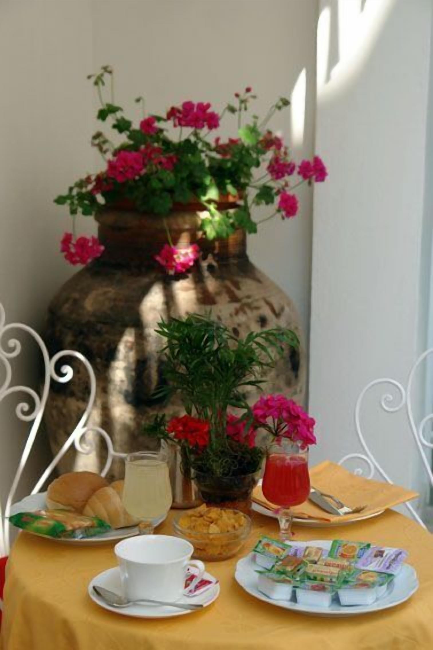Una tavola imbandita con una tazza bianca, un bicchiere di bevanda rossa, pasticcini e una pirotta di yogurt.