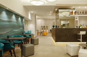 Un interior moderno con asientos azul verdosos y grises, una zona de bar con botellas y una pared grande con un diseño ondulado.
