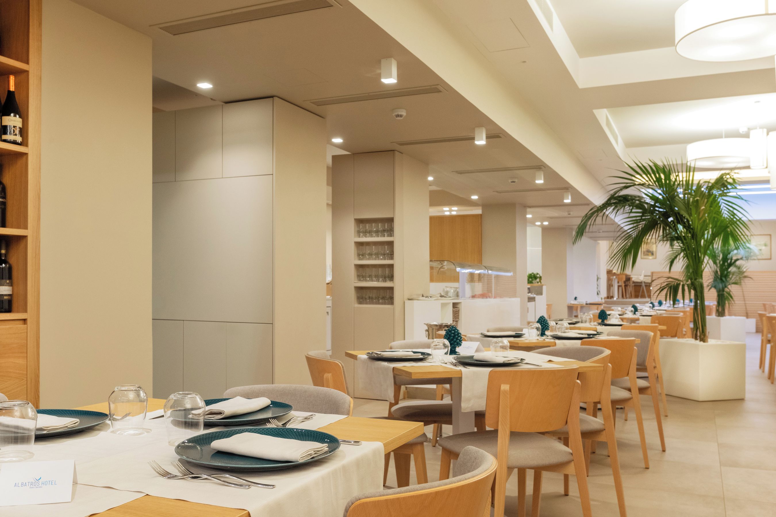 Une salle à manger d’hôtel avec plusieurs tables dressées pour les clients, équipées d’assiettes, de couverts et de verres.