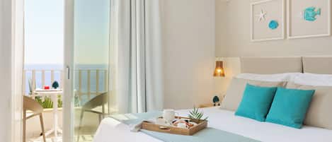 Una habitación de hotel con cama, una bandeja de desayuno, un balcón con una silla y vistas al mar.