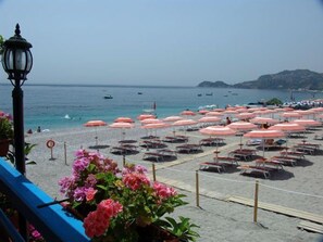 A beach with rows of pink umbrellas and lounge chairs, a clear view of the sea, and a lamp post in the foreground. - Albatros Beach Hotel - Letojanni (Letojanni)