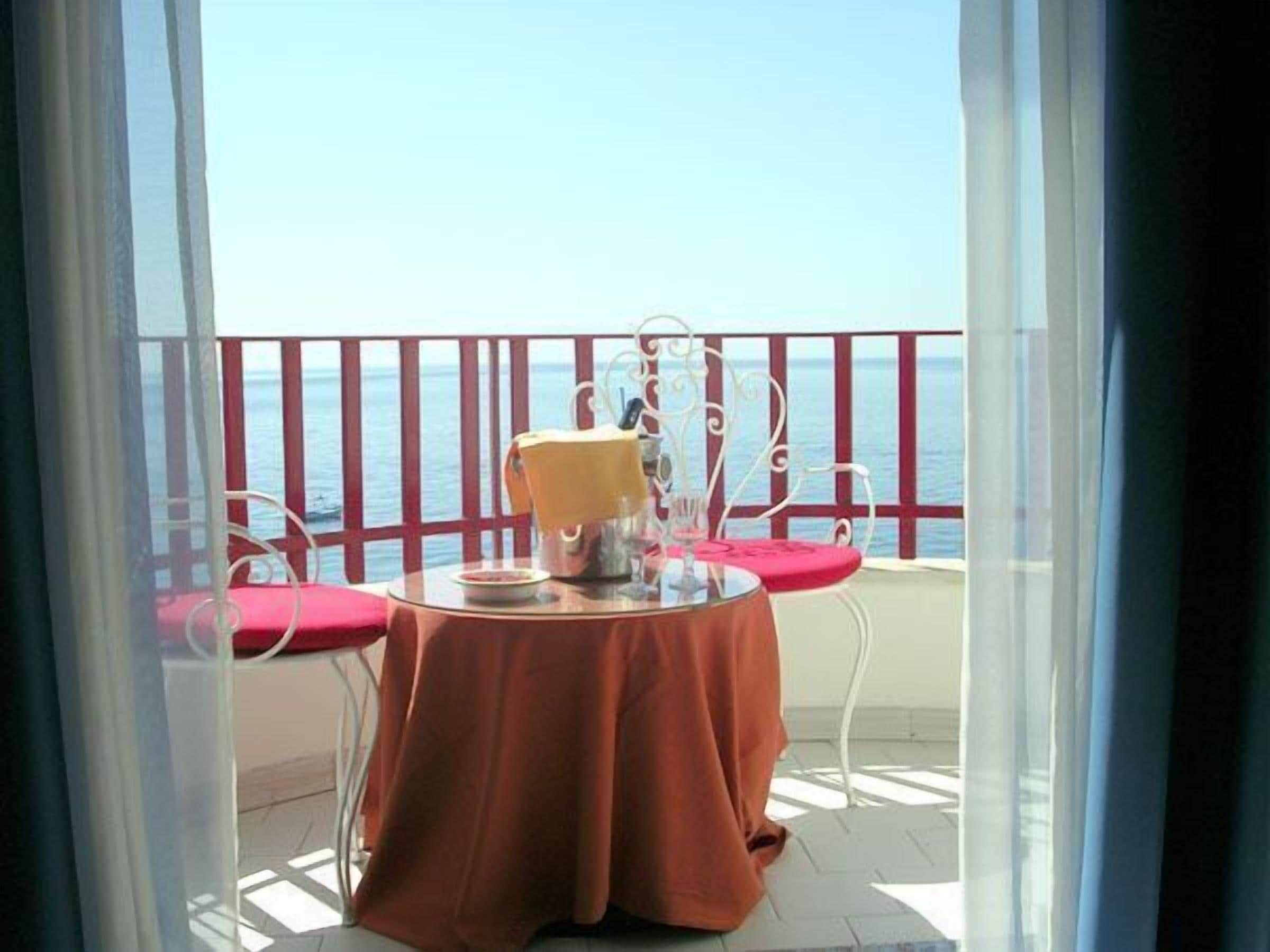 Un balcon avec une table dressée pour deux personnes, agrémentée d’une nappe rouge et de chaises blanches.
