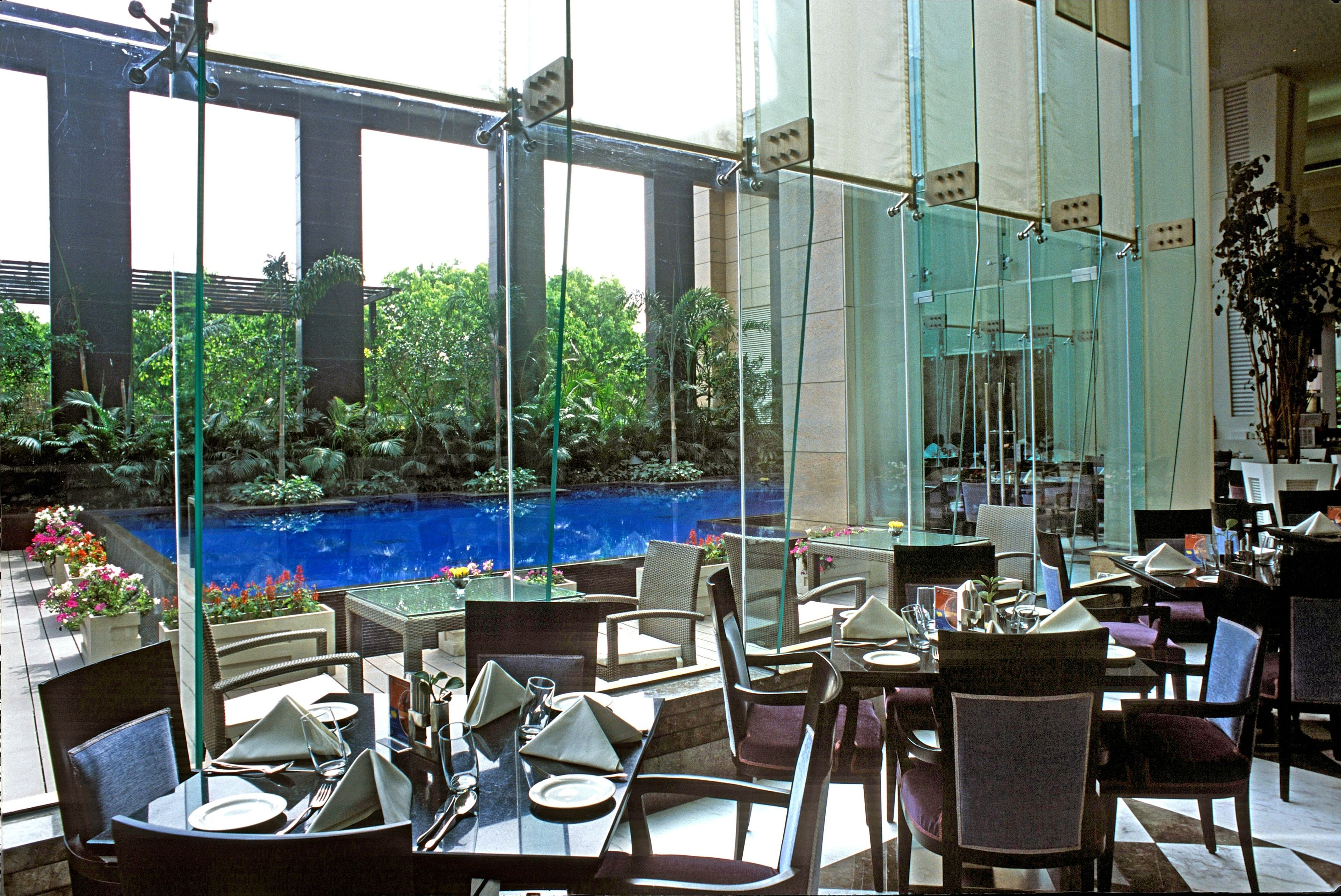 Un comedor interior con mesas y sillas, una pared de vidrio con vistas a un jardín y una piscina.