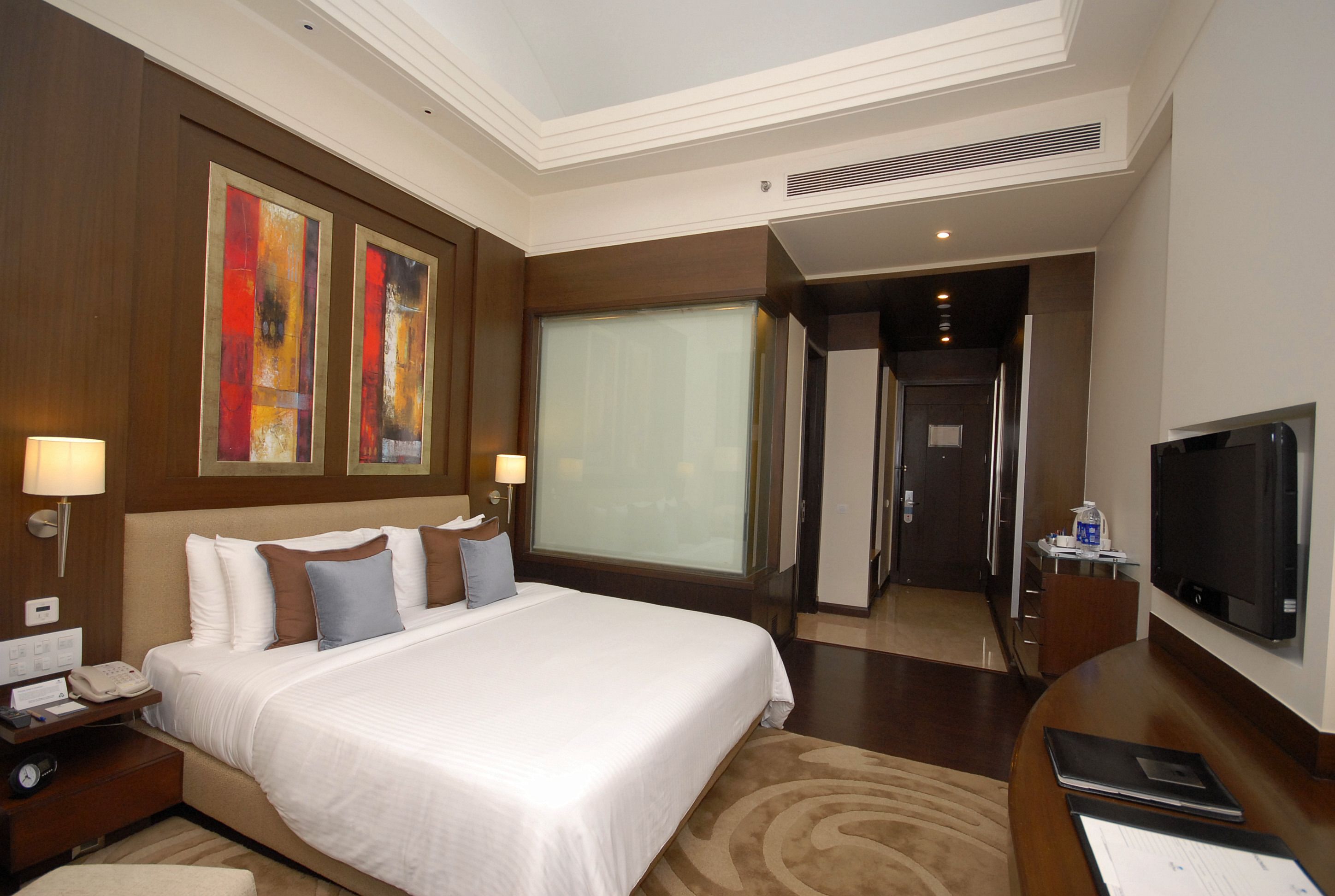 A hotel room with a large bed, bedside lamps, a flat-screen TV, and artwork on the wall.