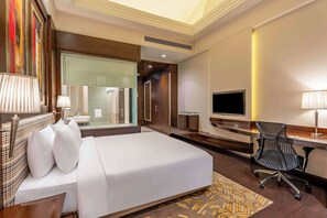 A hotel room with a large bed, a desk with a computer, a chair, and a television.