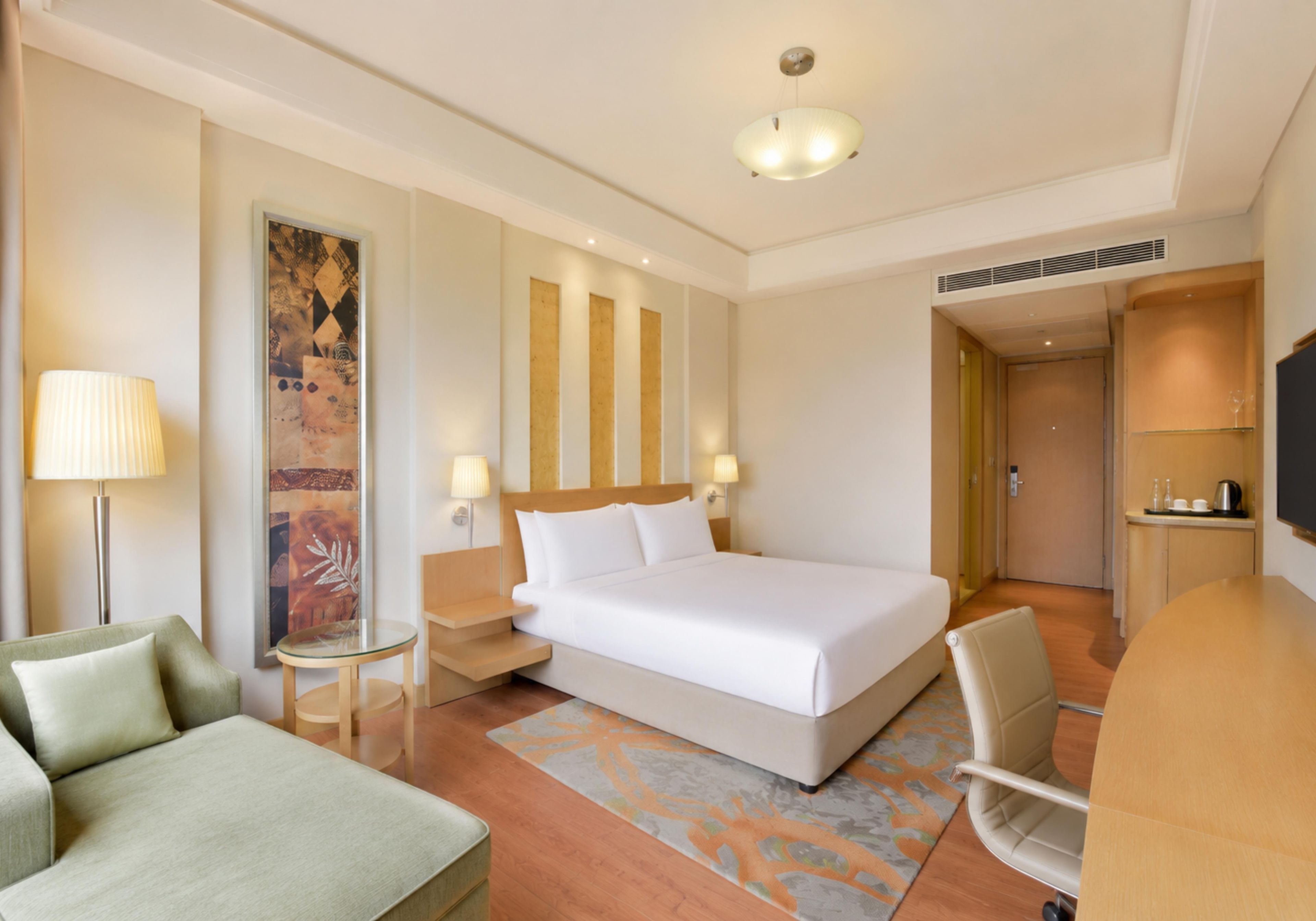 A hotel room with a large bed, a desk, a chair, a lamp, and a painting on the wall.
