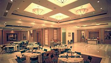 Une salle de banquet spacieuse, dotée de nombreuses tables rondes dressées pour le repas, avec des chaises et une décoration de table soignée.