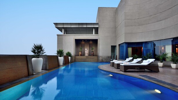 A modern outdoor pool area with lounge chairs and potted plants. - Radisson Noida (Noida)