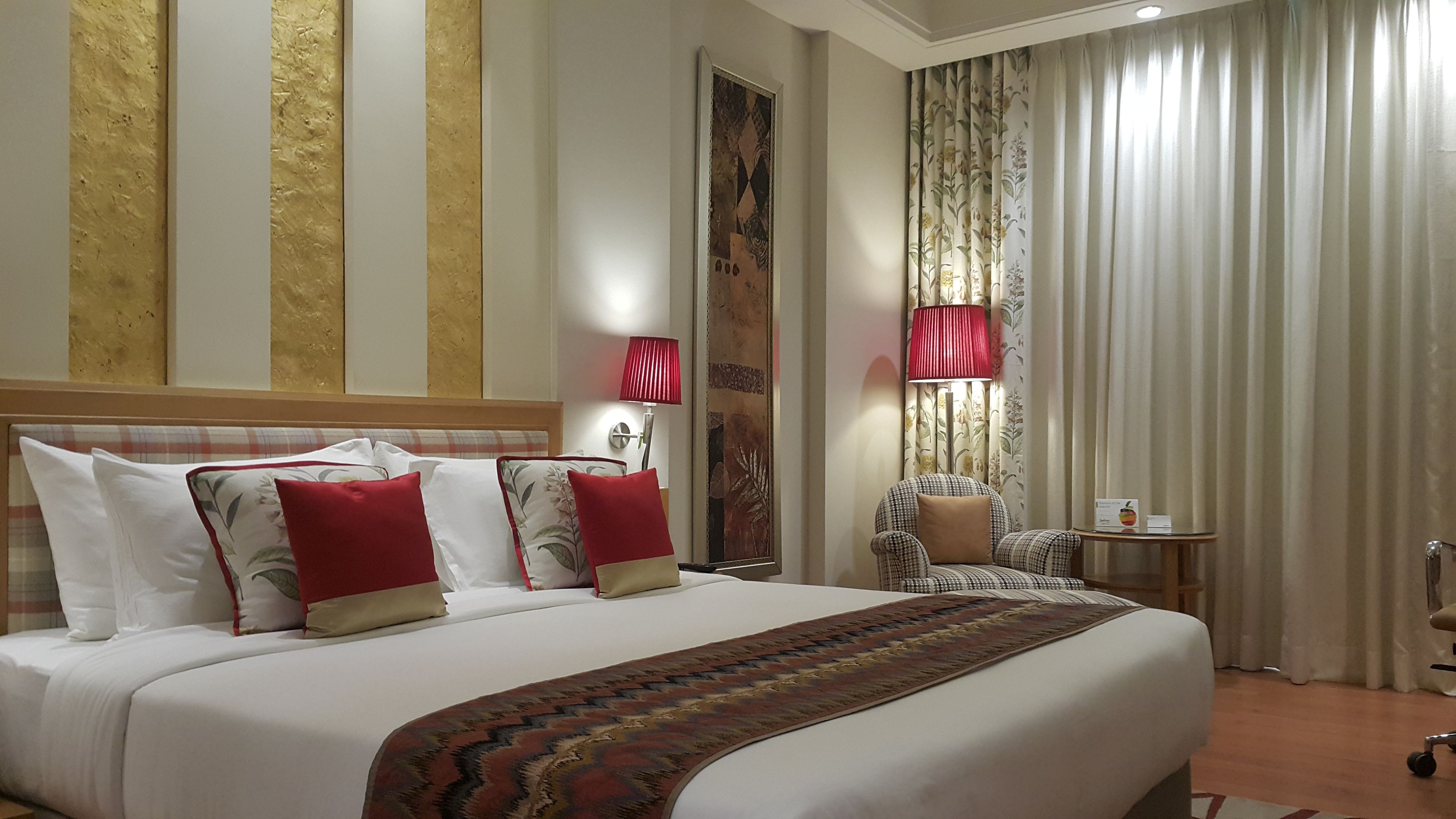 Een hotelkamer met een groot bed, een stoel, een klein tafeltje en gordijnen.