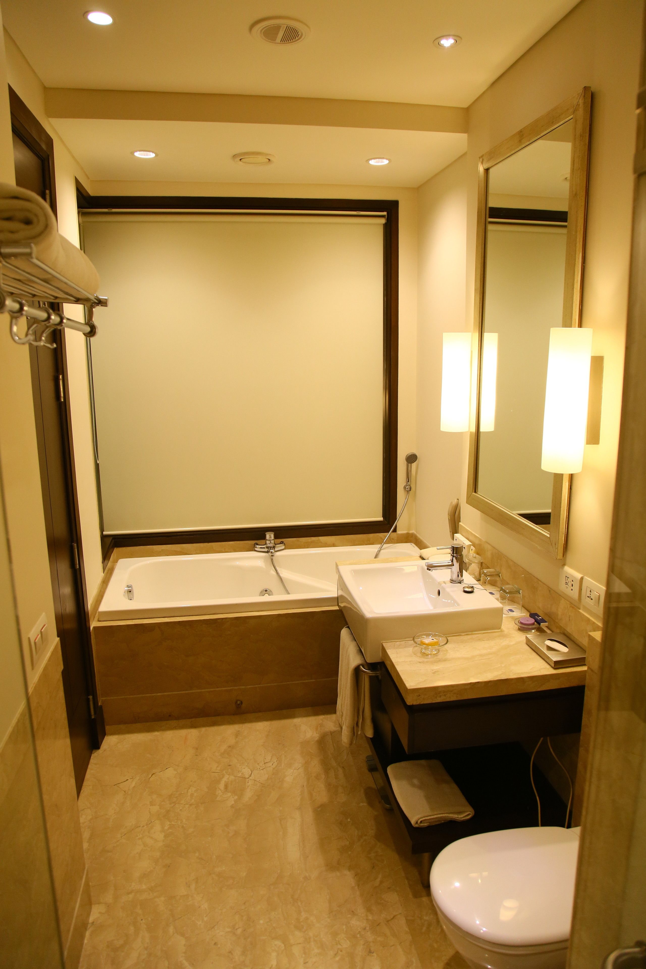 A compact hotel bathroom with a bathtub, two sinks, a toilet, and a large mirror.