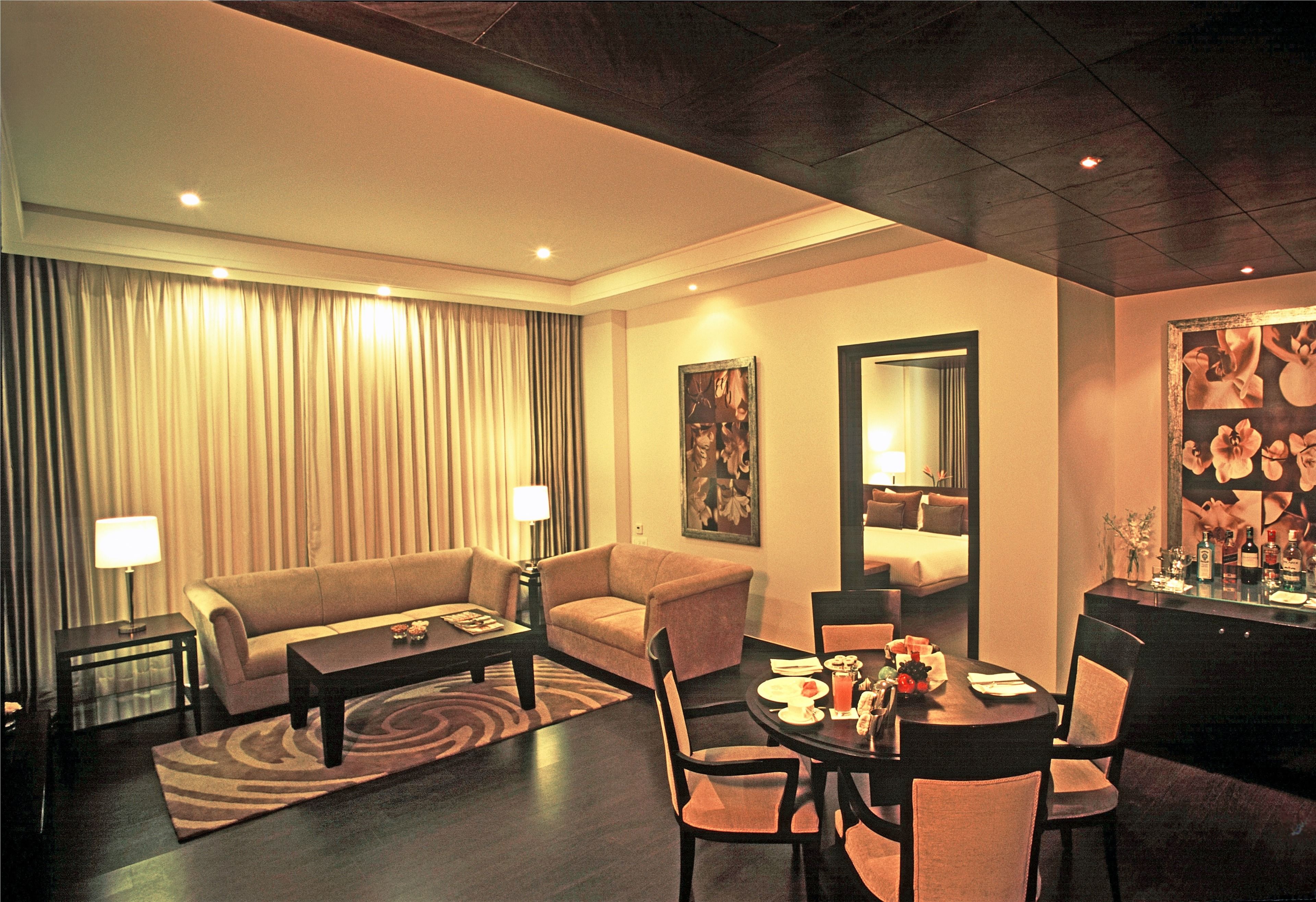 Une chambre d’hôtel comprenant un coin salon, une table à manger avec des chaises, un canapé, une table basse, une lampe et un grand miroir.