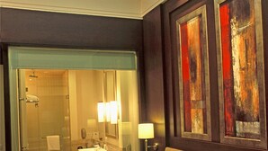 A hotel room with a large bed, a bathroom with a glass shower enclosure, and artwork on the walls. - Radisson Noida (Noida)