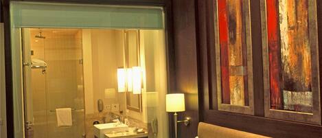 Habitación de hotel con una cama grande, baño con cabina de ducha de vidrio y obras de arte en las paredes.