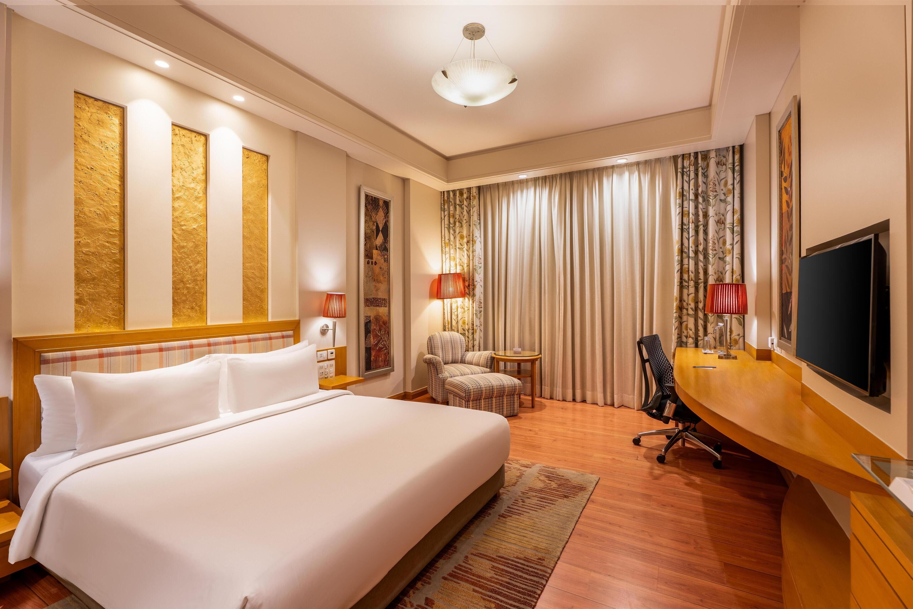 A hotel room with a large bed, a desk, a chair, a television, and a window with curtains.