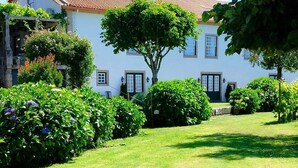 A white building with a red-tiled roof, surrounded by lush greenery and a well-maintained lawn. - Casa de Santa Ana da Beira (Seia)