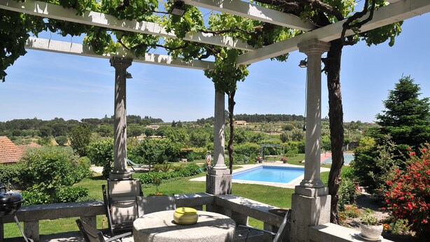 A pergola with a table and chairs, overlooking a pool and lush greenery. - Casa de Santa Ana da Beira (Seia)