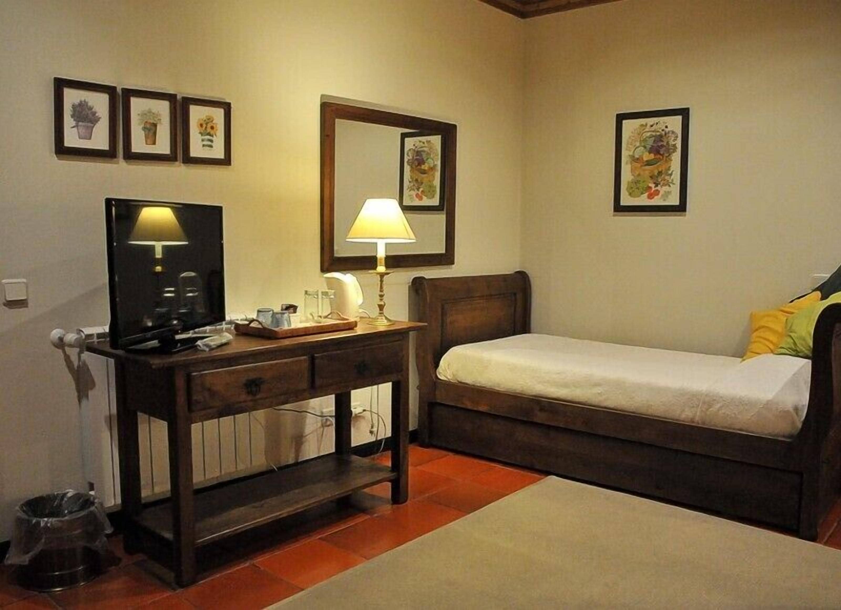 Une chambre à coucher avec un lit, un bureau avec une lampe, une télévision et des tableaux encadrés accrochés au mur.