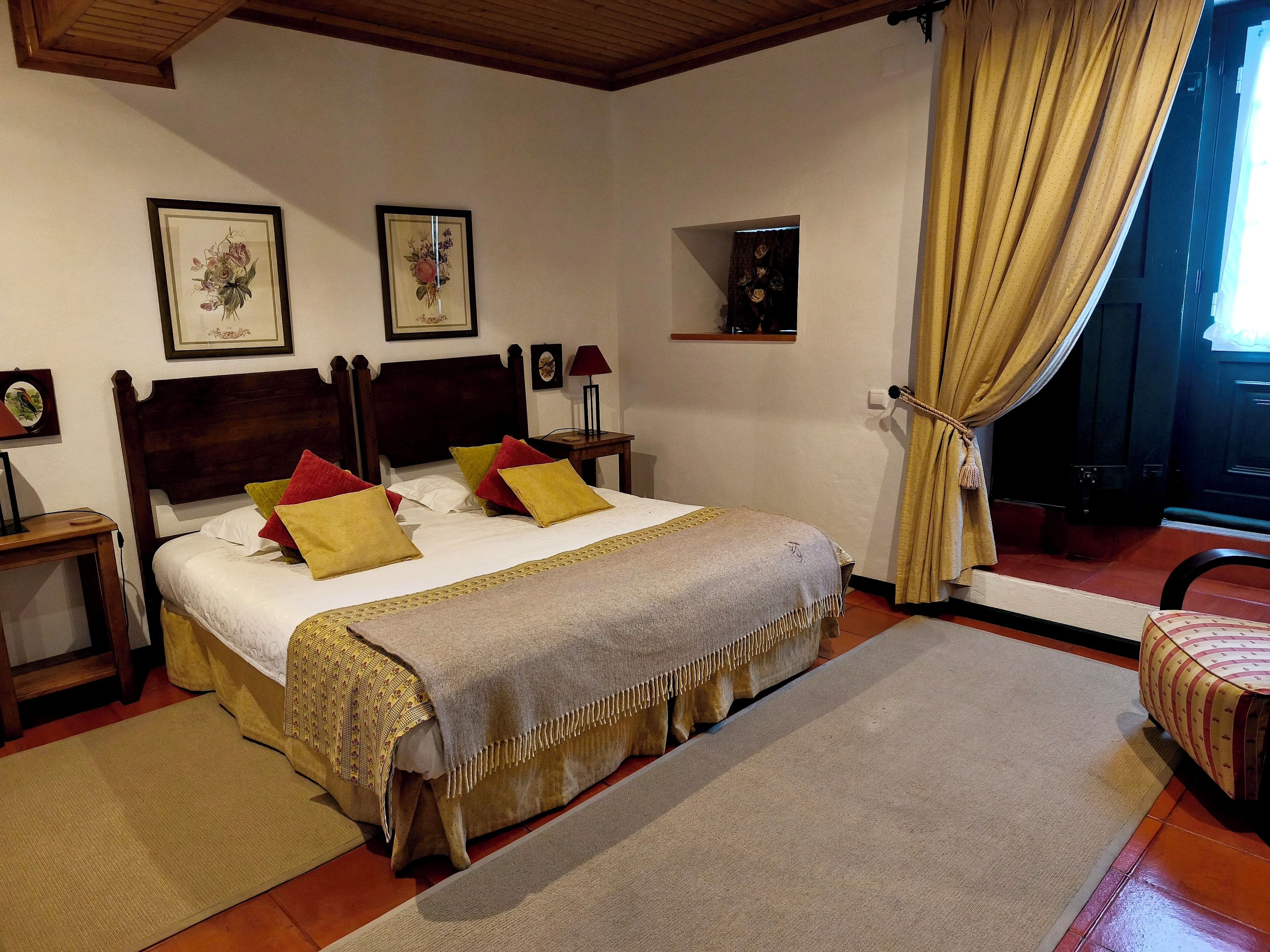 A neatly arranged bedroom with a large bed, a bedside table, a small shelf, and a window with curtains.