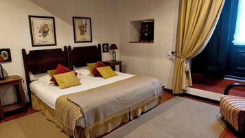 A neatly arranged bedroom with a large bed, a bedside table, a small shelf, and a window with curtains.