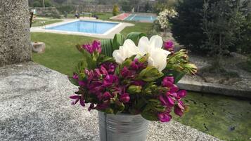 A flower arrangement in a metal pot on a stone ledge with a view of a swimming pool and tennis courts in the background.