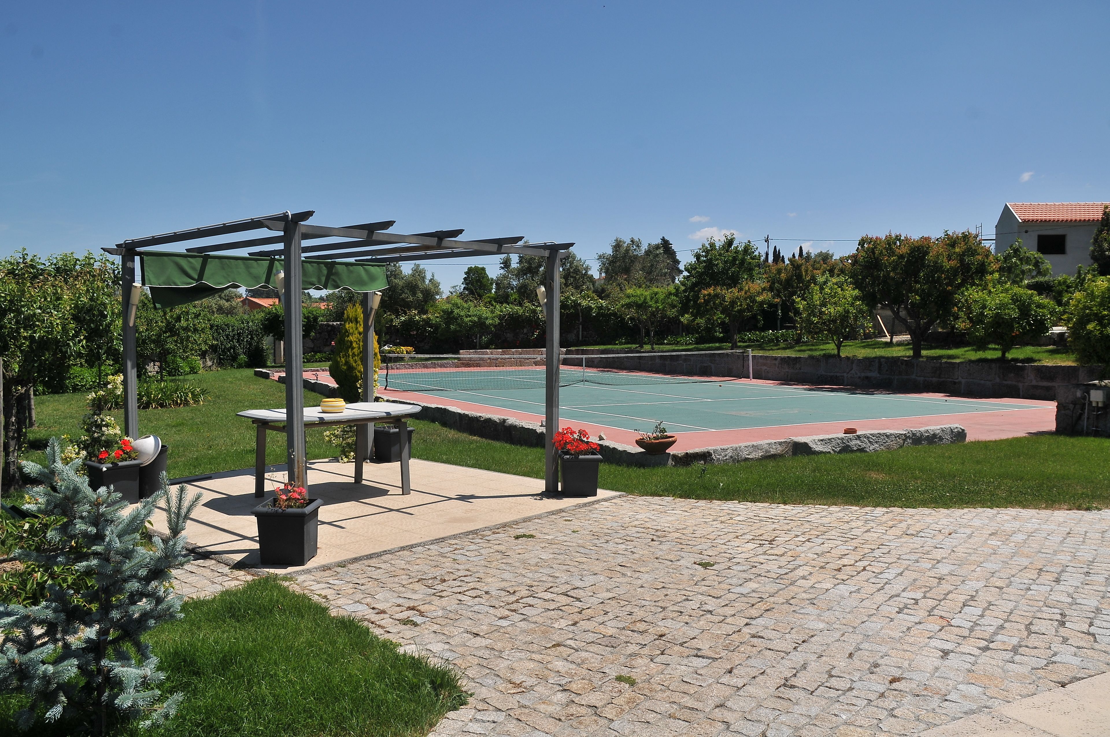 Un court de tennis extérieur doté d’une pergola, d’un espace détente et de plantes en pot.
