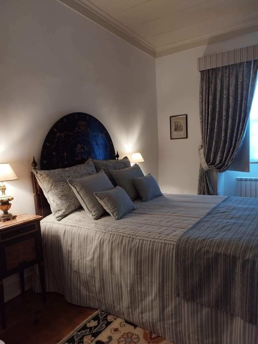 A bedroom with a large bed, a headboard with a circular design, two bedside lamps, and a framed picture on the wall.