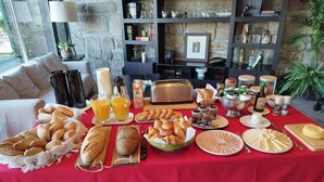 A breakfast buffet with various breads, pastries, and beverages on a red tablecloth. - Casa de Santa Ana da Beira (Seia)