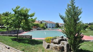 A tennis court surrounded by greenery and a stone wall, with a building in the background.