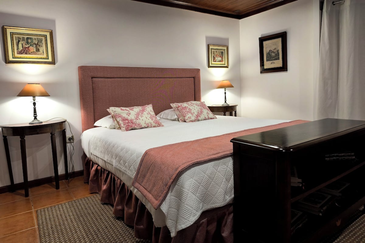 Une chambre à coucher bien rangée, avec un grand lit, deux tables de chevet dotées de lampes et des tableaux encadrés accrochés aux murs.