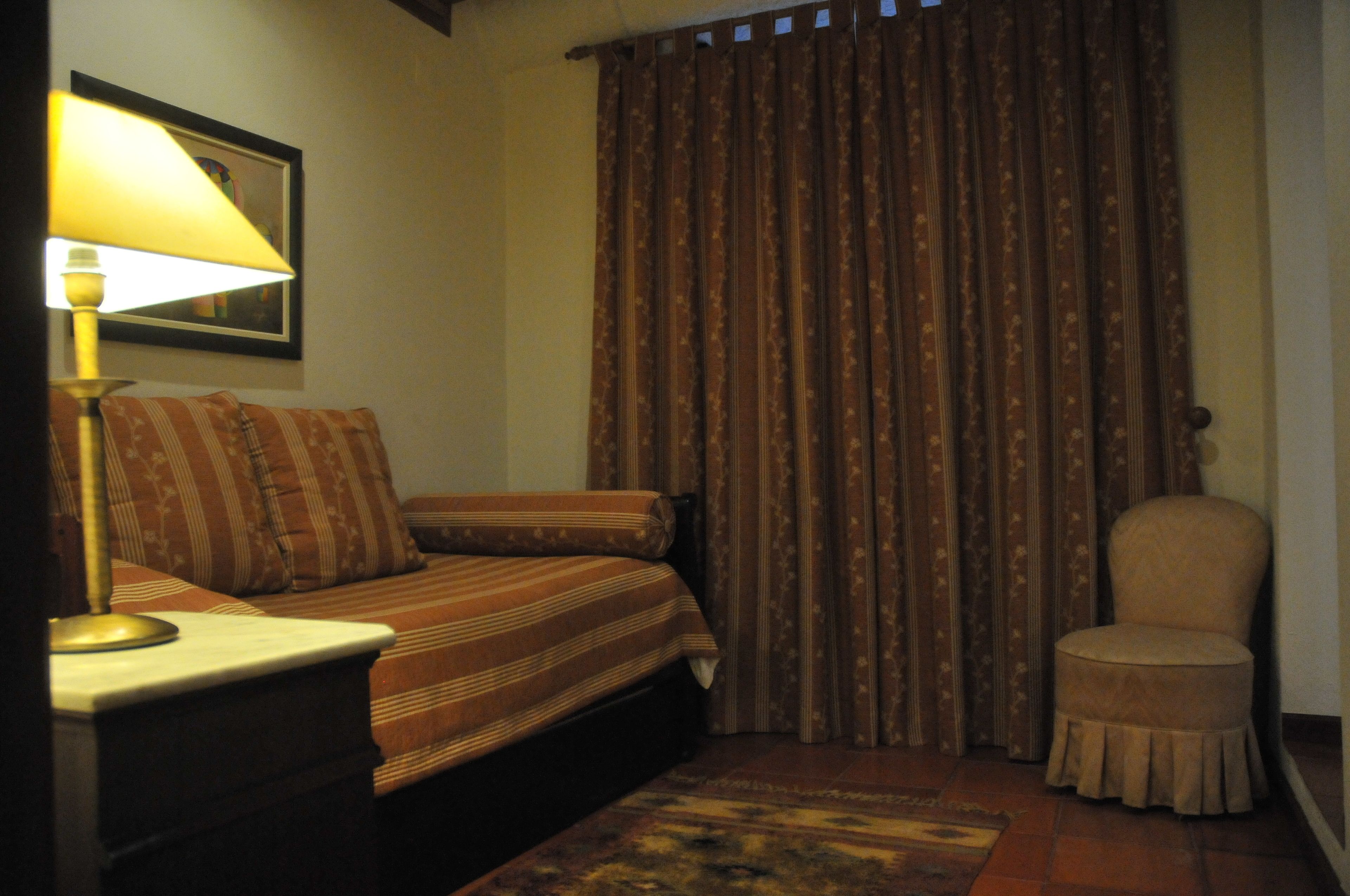 A bedroom with a bed, a chair, a lamp, and a curtain.