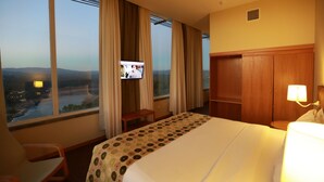 Habitación de hotel con cama, escritorio, silla, televisión y vistas a la ciudad.