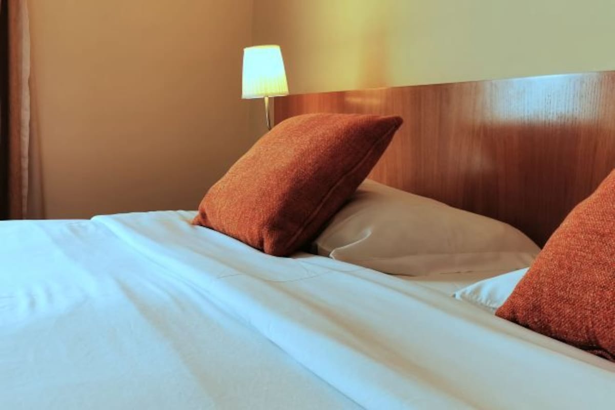 Una cama bien tendida con sábanas blancas y dos almohadas marrones.