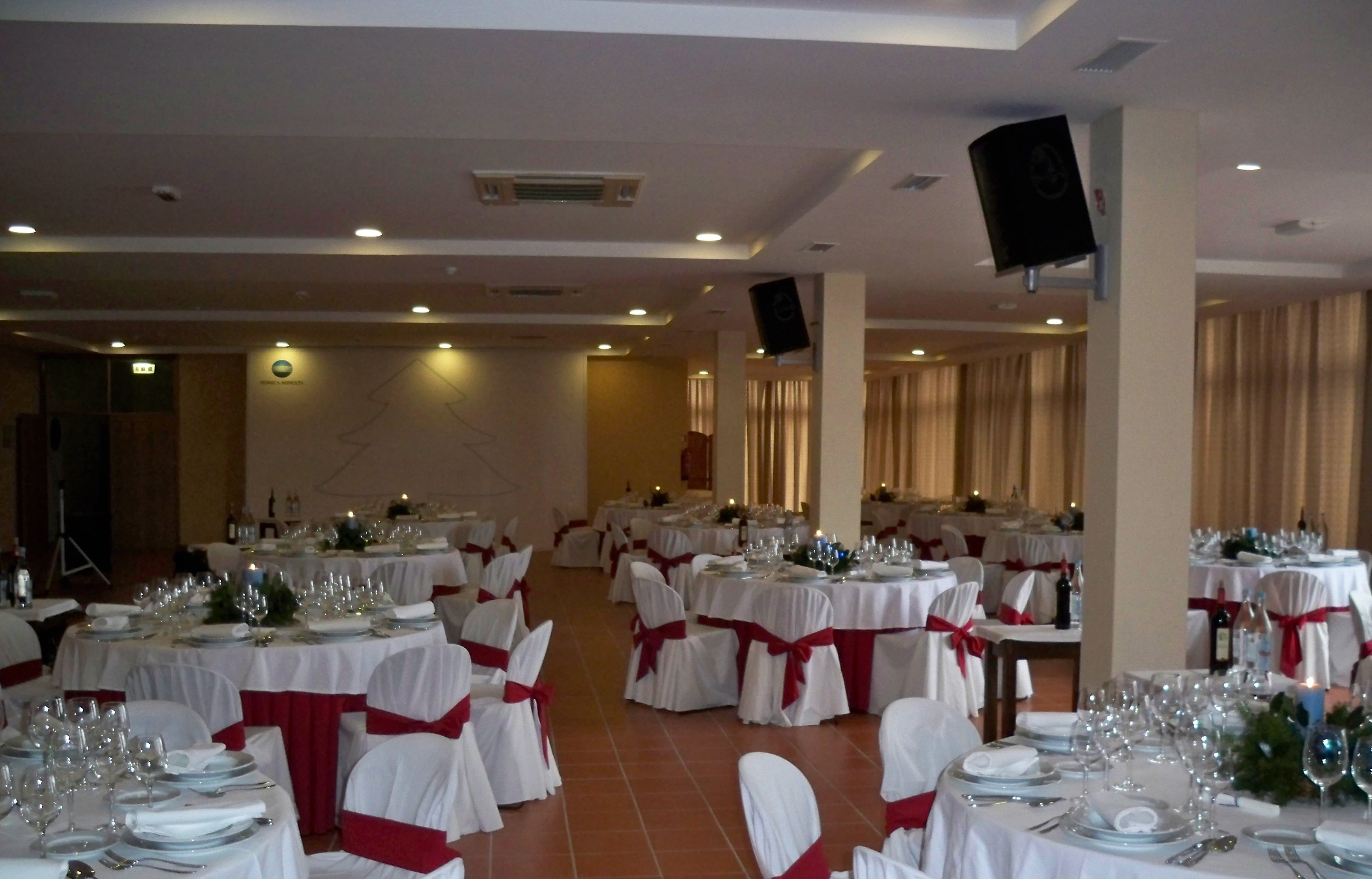 A banquet hall with round tables set for dining, white tablecloths, and red sashes.
