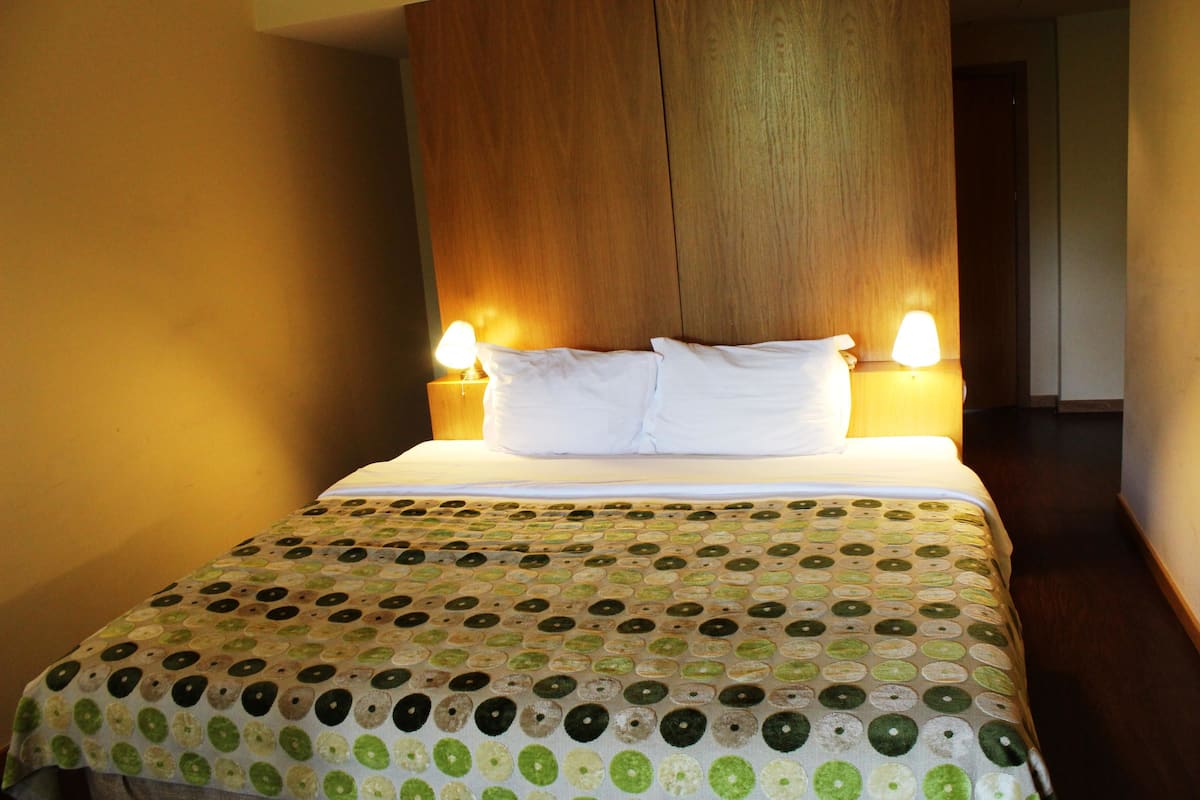 A neatly made bed with a patterned bedspread, two bedside lamps, and a wooden headboard.