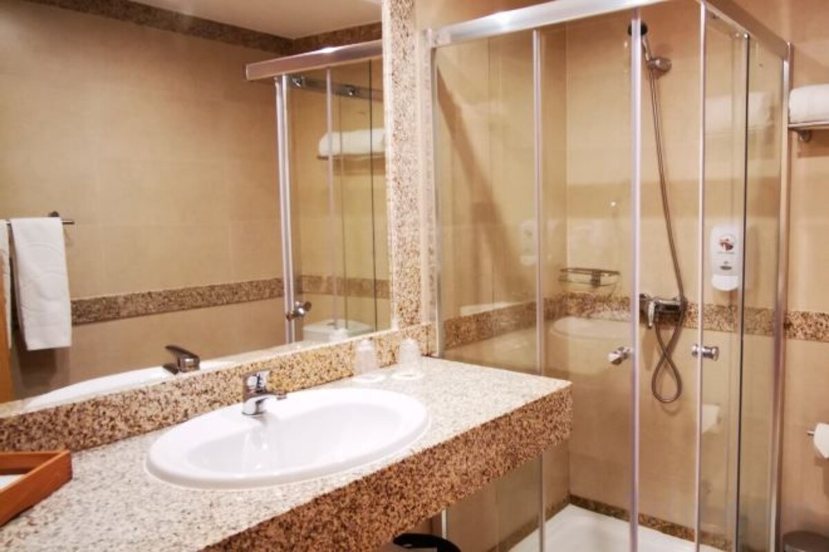 A bathroom with a sink, mirror, shower, and glass-enclosed shower stall.